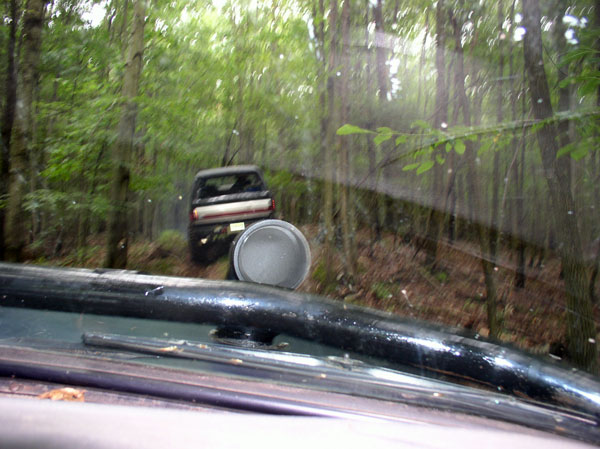 Dark SUV driving on a dirt path in a forest, seen from inside another vehicle