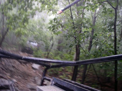 1988 Ford Bronco - A white SUV navigates a challenging dirt path through a dense, green forest during what appears to be rainy weather.