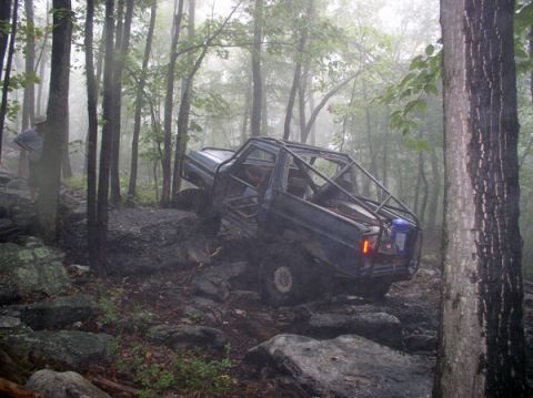 1988 Ford Bronco - An off-road vehicle with a custom roll cage tackles a challenging rocky trail in a foggy forest.