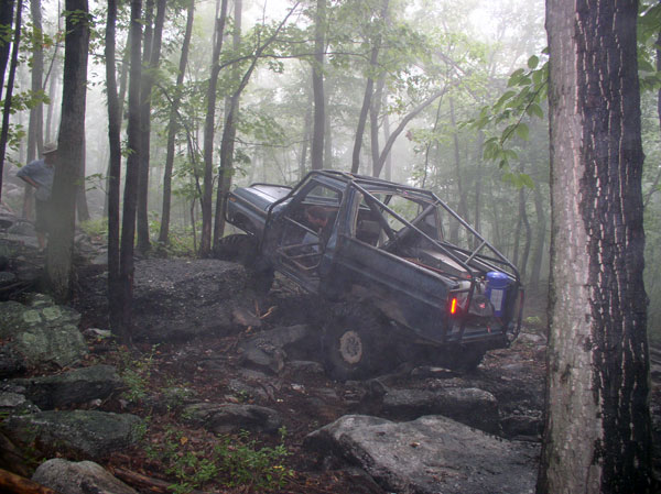 Dark blue off-road vehicle with a roll cage navigating rocky terrain