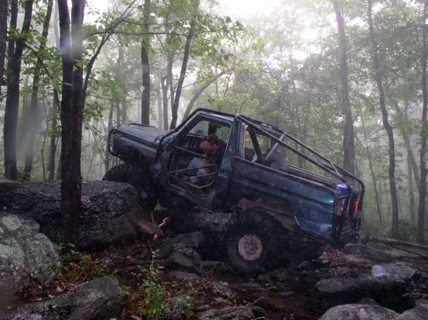 Blue off-road SUV with roll cage navigating rocky terrain