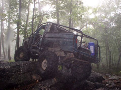 1988 Ford Bronco - This heavily modified SUV navigates a challenging trail in a foggy, wooded environment.