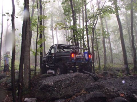 1988 Ford Bronco - An off-road vehicle navigates a challenging rocky path through a misty forest.