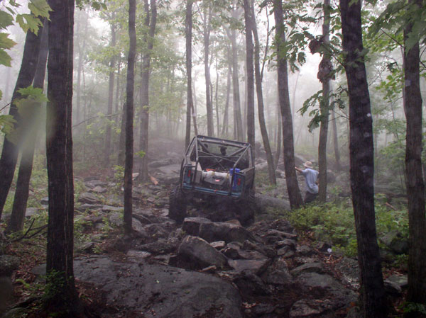 Off-road vehicle with roll cage on a rocky trail in a misty forest