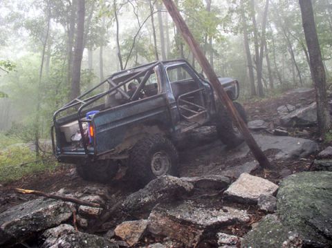 1988 Ford Bronco - A modified off-road vehicle tackles a challenging trail in a foggy forest.