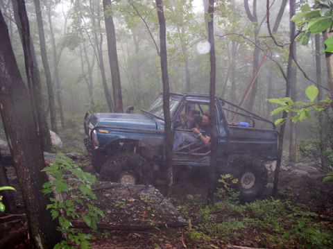 1988 Ford Bronco - Off-road truck with custom roll cage navigates a rocky, wooded trail.