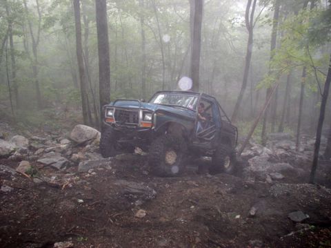 1988 Ford Bronco - This modified Ford Bronco navigates a challenging, rocky trail in a foggy forest.
