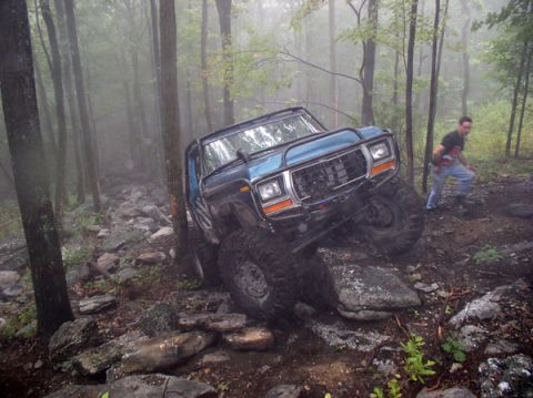1988 Ford Bronco - A blue off-road SUV tackles a challenging rocky path in a foggy forest.