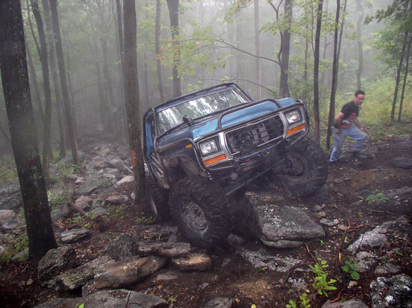 Blue off-road SUV with a brush guard navigating a rocky, wooded trail