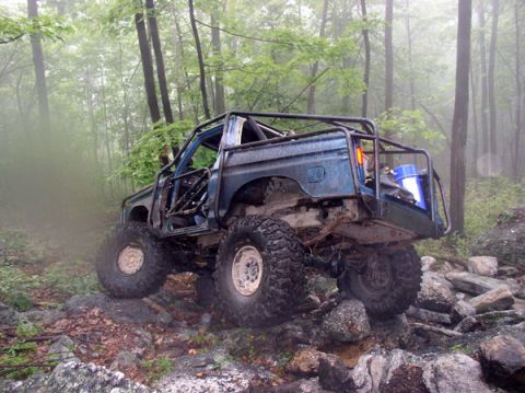 1988 Ford Bronco - This heavily modified SUV navigates a rocky trail in a misty forest environment.