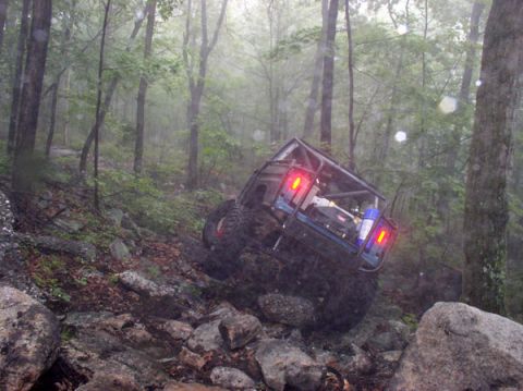 1988 Ford Bronco - A modified off-road vehicle navigates a steep, rocky trail in a foggy forest.