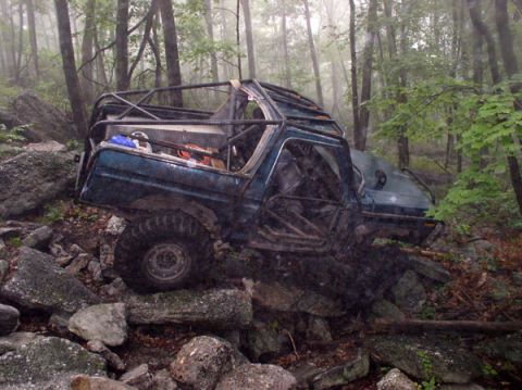1988 Ford Bronco - Modified off-road SUV navigating a challenging rocky trail in a misty forest.