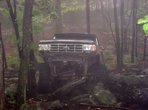 1988 Ford Bronco - A modified black Ford Bronco tackles a challenging off-road course amidst trees and fog.