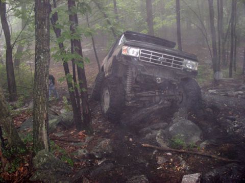 1988 Ford Bronco - A modified Ford Bronco navigates a rocky, wooded off-road course on a foggy day.