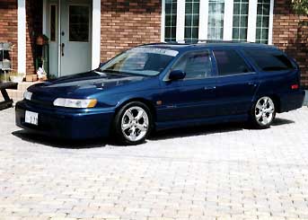 1990 Mercury Sable - A blue station wagon is parked in front of a brick building.