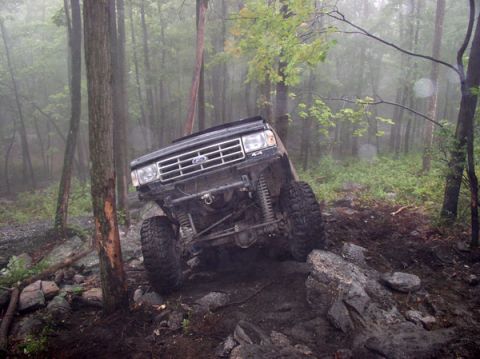 1988 Ford Bronco - A lifted Ford Bronco navigates a rocky trail in a foggy forest setting.