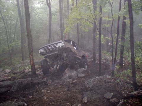 1988 Ford Bronco - A lifted Ford Bronco navigates a challenging rocky path through a misty forest.