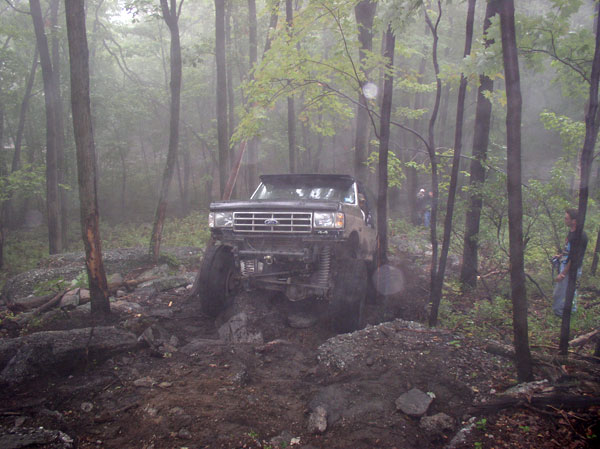 Ford Bronco with lifted suspension driving through mud and rocks in a forest