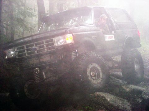 1988 Ford Bronco - A 1988 Ford Bronco navigates a rocky trail in a foggy, wooded environment.