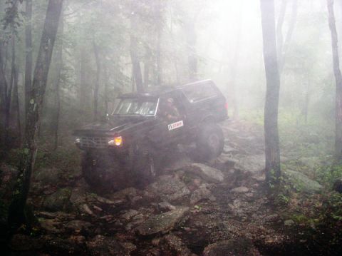 1988 Ford Bronco - A black SUV navigates a challenging, rocky trail through a misty forest.