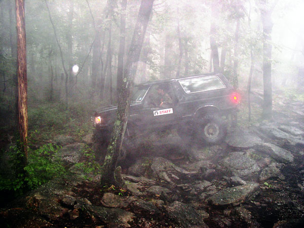 Dark lifted SUV with STAFF sign on rear window descending a foggy rocky trail