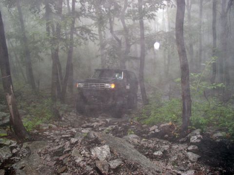 1988 Ford Bronco - Ford Bronco driving through a rocky, wooded area on a foggy day.