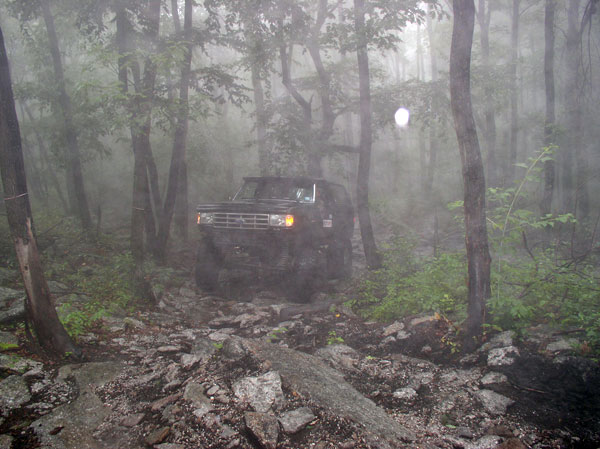 1987 Ford Bronco navigating a rough, forested path with fog