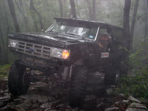 1988 Ford Bronco - A black Ford Bronco navigates a challenging, rocky path through a misty forest.