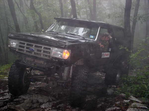 Black Ford Bronco on rocky trail in foggy woods, driver visible