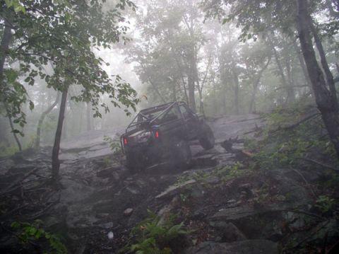 1988 Ford Bronco - Off-road vehicle navigates a challenging rocky path through a foggy forest.