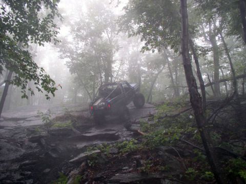 1988 Ford Bronco - An off-road vehicle navigates a challenging, wet terrain amidst trees and fog.