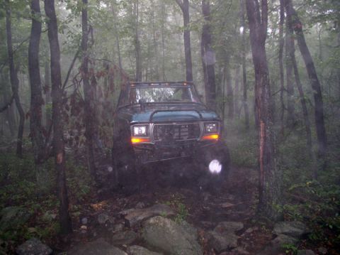 1988 Ford Bronco - Ford Bronco driving through a wooded area with fog and rocks.
