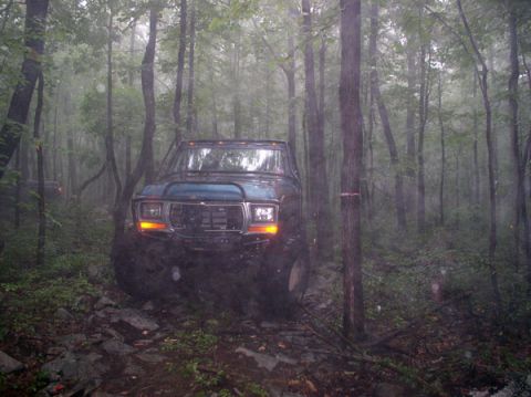 1988 Ford Bronco - A lifted Ford Bronco navigates a challenging, wet forest trail.