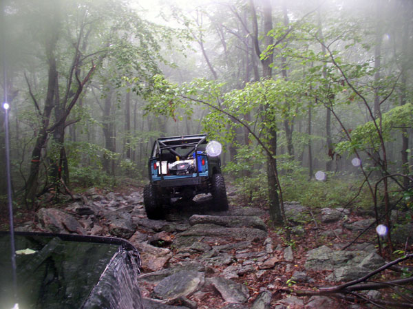 Blue off-road SUV with roll cage driving on a rocky trail in a foggy forest