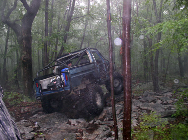 Blue off-road SUV with roll cage navigating rocky terrain