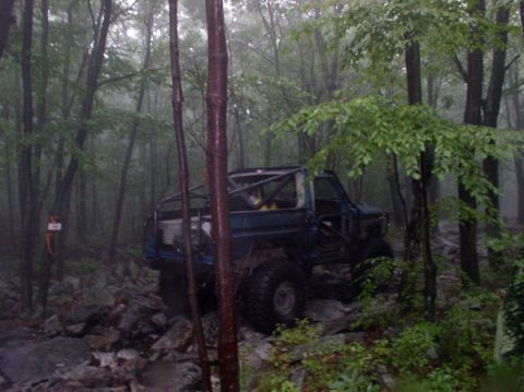1988 Ford Bronco - Modified 1988 Ford Bronco navigating a difficult off-road course in a wooded area.
