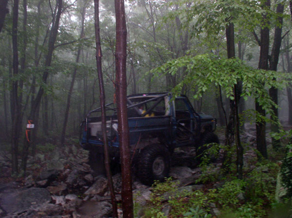 Blue 1988 Ford Bronco with roll cage on rocky forest trail