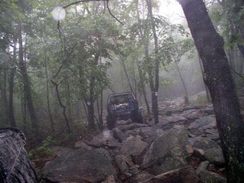1988 Ford Bronco - An off-road vehicle traverses a challenging, rocky path through a misty forest.