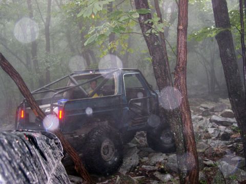 1988 Ford Bronco - Off-road vehicle with roll cage navigating a rocky trail in a forest.