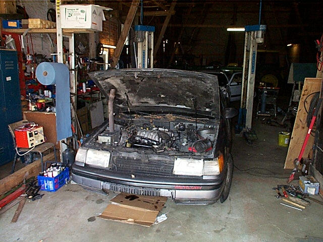 Gray Mercury sedan with hood open showing engine bay inside a garage workshop