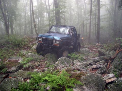 1988 Ford Bronco - This modified SUV navigates a challenging, rocky path through a misty wooded area.
