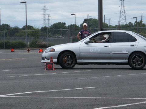 2001 Mercury Grand Marquis - A silver sedan navigates a course marked by traffic cones, with a driver wearing a helmet visible inside.