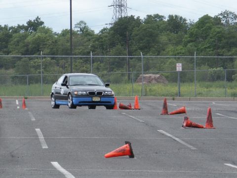 2001 Mercury Grand Marquis - A black BMW 3 Series sedan with distinctive blue lower body panels is seen on a paved lot, maneuvering through an obstacle course marked by…