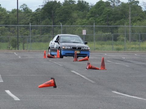 2001 Mercury Grand Marquis - A dark BMW 3 Series sedan with distinctive blue lower body panels maneuvers through an autocross course marked by orange cones.