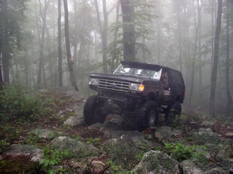 1988 Ford Bronco - A lifted Ford Bronco navigates a rocky trail in a misty wooded area.