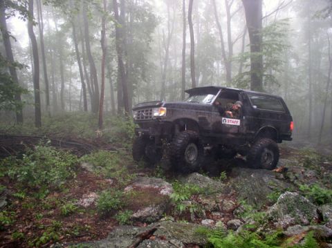 1988 Ford Bronco - A black Ford Bronco navigates a challenging off-road course amidst a foggy forest.