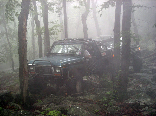 Green doorless 4x4 with brush guard and roll cage crawling wet rocks in thick fog