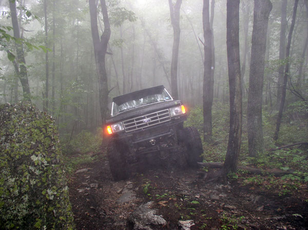Black Ford Bronco off-roading on a foggy forest trail, front grille visible