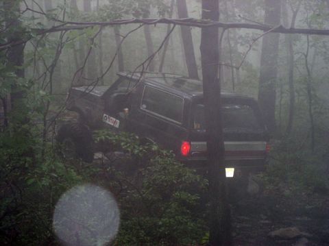 1988 Ford Bronco - A black 1988 Ford Bronco navigates a foggy, wooded trail, its tires gripping the terrain.