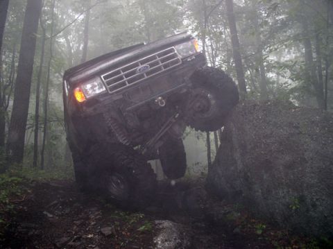1988 Ford Bronco - A black Ford Bronco navigates a challenging off-road course in a misty woodland environment.
